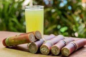 raw sugarcane chopped in to smaller pieces and a glass of sugarcane juice