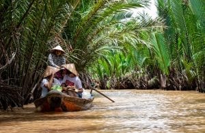 Small boat travelling down the Mekong, with high sided planting either side of the river 