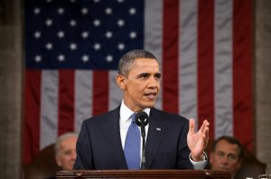 Barack Obama in front of the US Flag, talking to the room