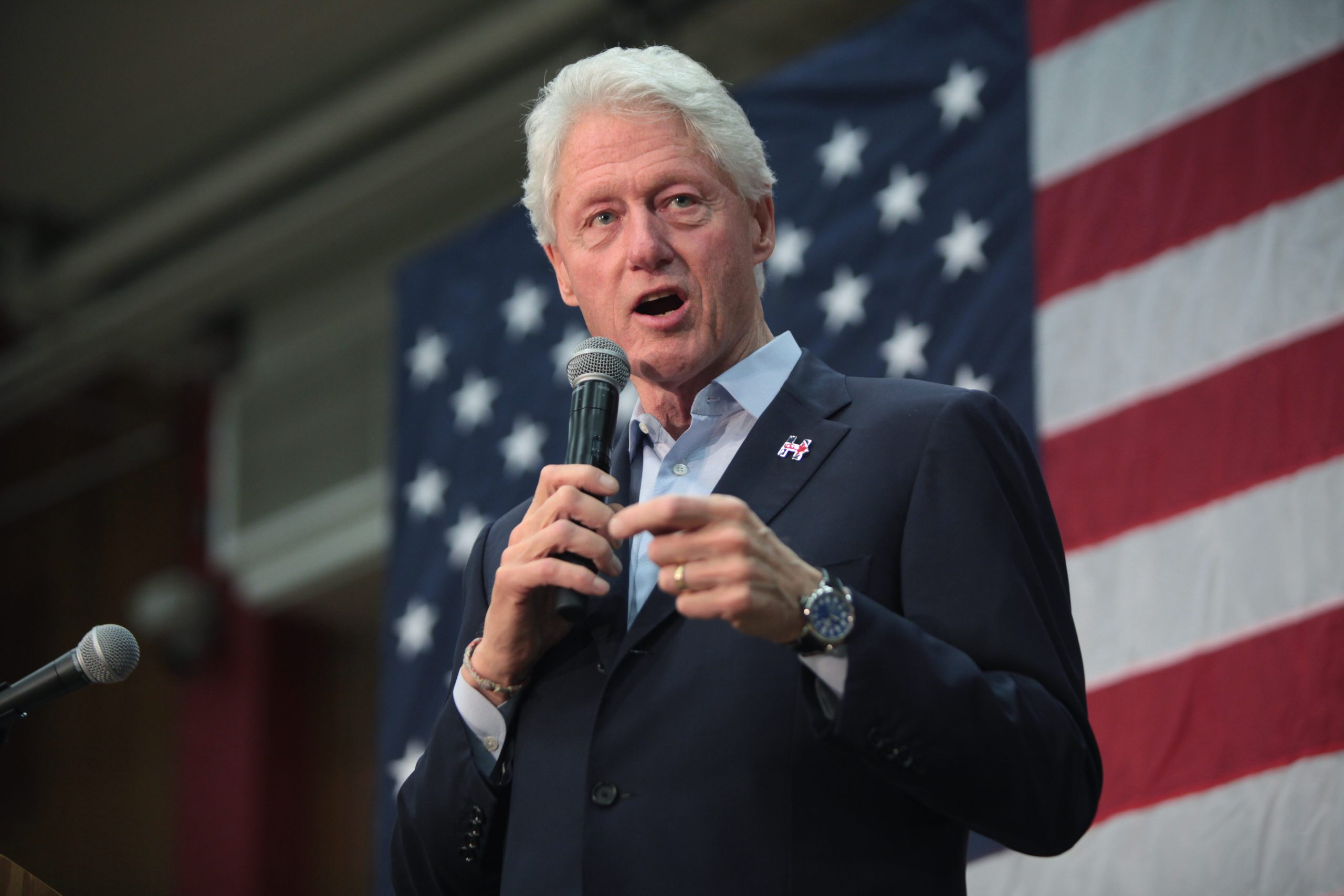 Bil Clinton on stage in front on the USA Flag, speaking to the crowd