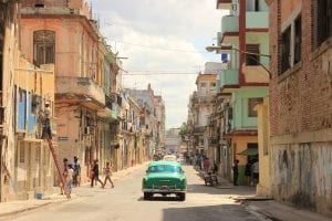 A vintage car travelling down a dusty looking street in Havana