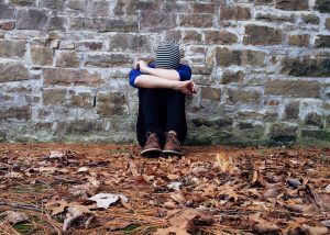 a man sat against a wall crying in to his knees