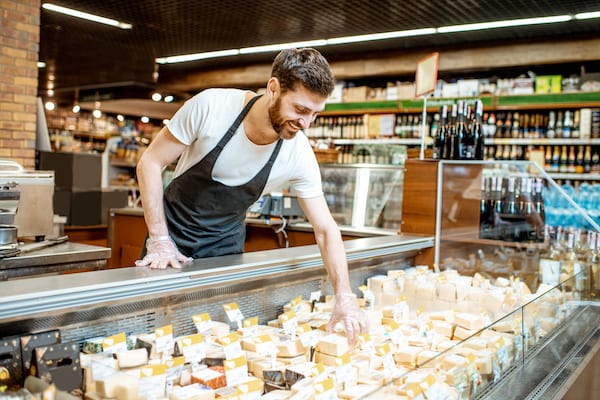 Shop worker laying out cheese pieces into the refrigeration showcase in the supermarket