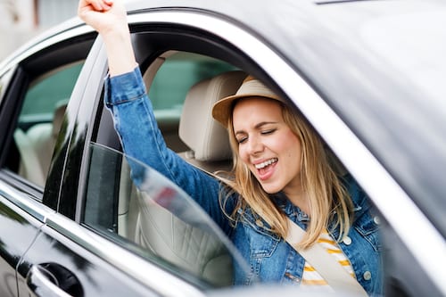 A young woman listening to music and dancing in the car